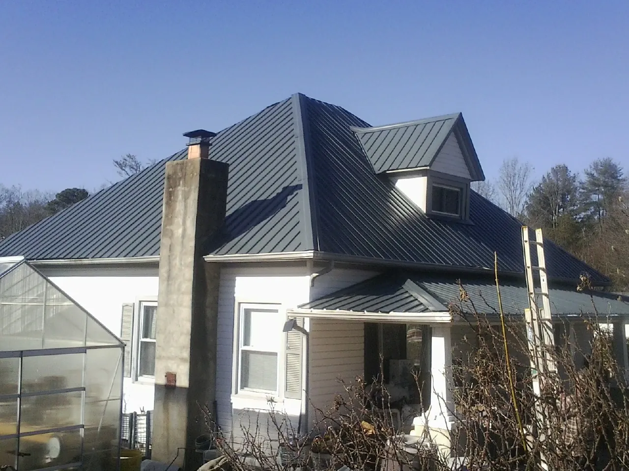 Dark blue standing seam metal roof on a white farmhouse with dormer — Slate & Tile Roof Repair by Roofing Brothers in Van Hornesville