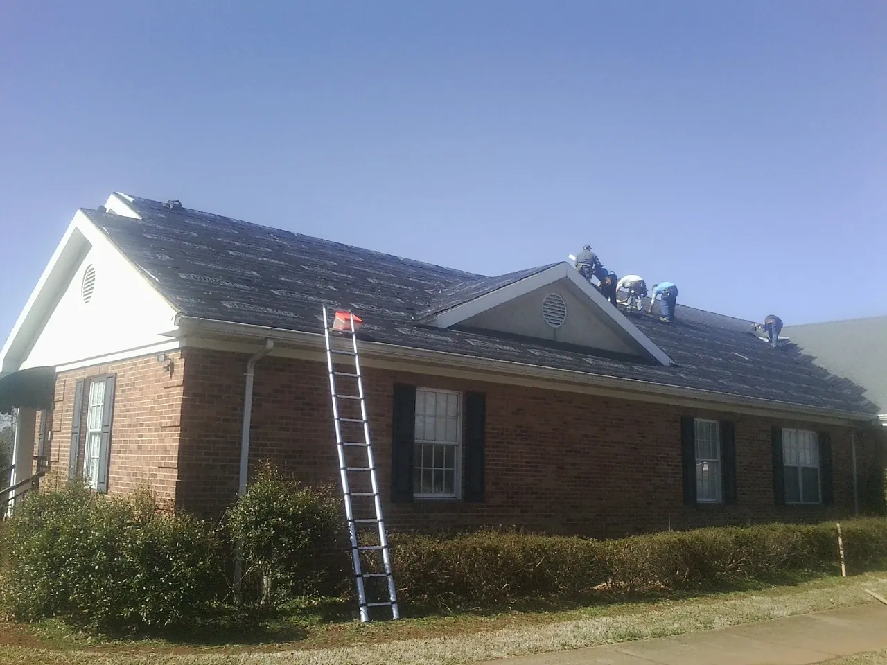 Crew tearing shingles off a brick ranch roof with a ladder set — Metal Roof Repair work by our crew in Van Hornesville