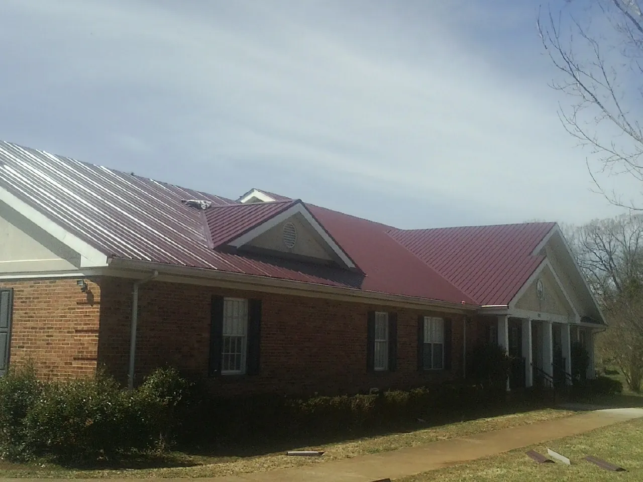 Red metal roof with gabled entries on a long brick building, from a Hail Damage Roof Repair job in Van Hornesville