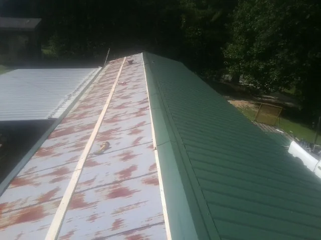 Old rusted panels beside newly installed green metal roofing — Wind Damage Roof Repair by Roofing Brothers in Van Hornesville