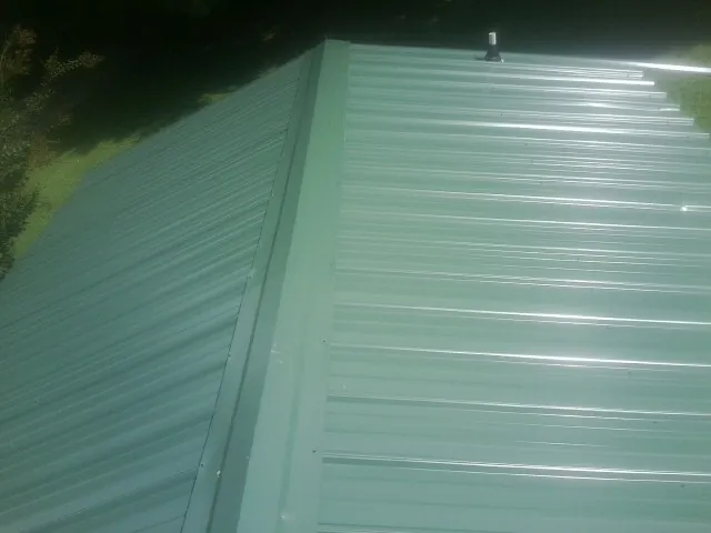 New green metal panels meeting at the ridge of a roof — Flat Roof Repair work by our crew in Van Hornesville