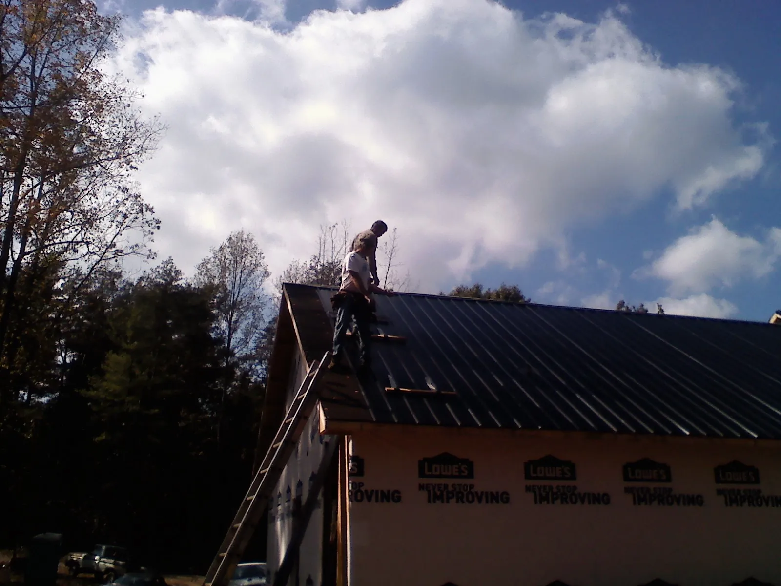 Roofer fastening dark metal panels high against a cloudy sky, from a Roof Inspection job in Van Hornesville