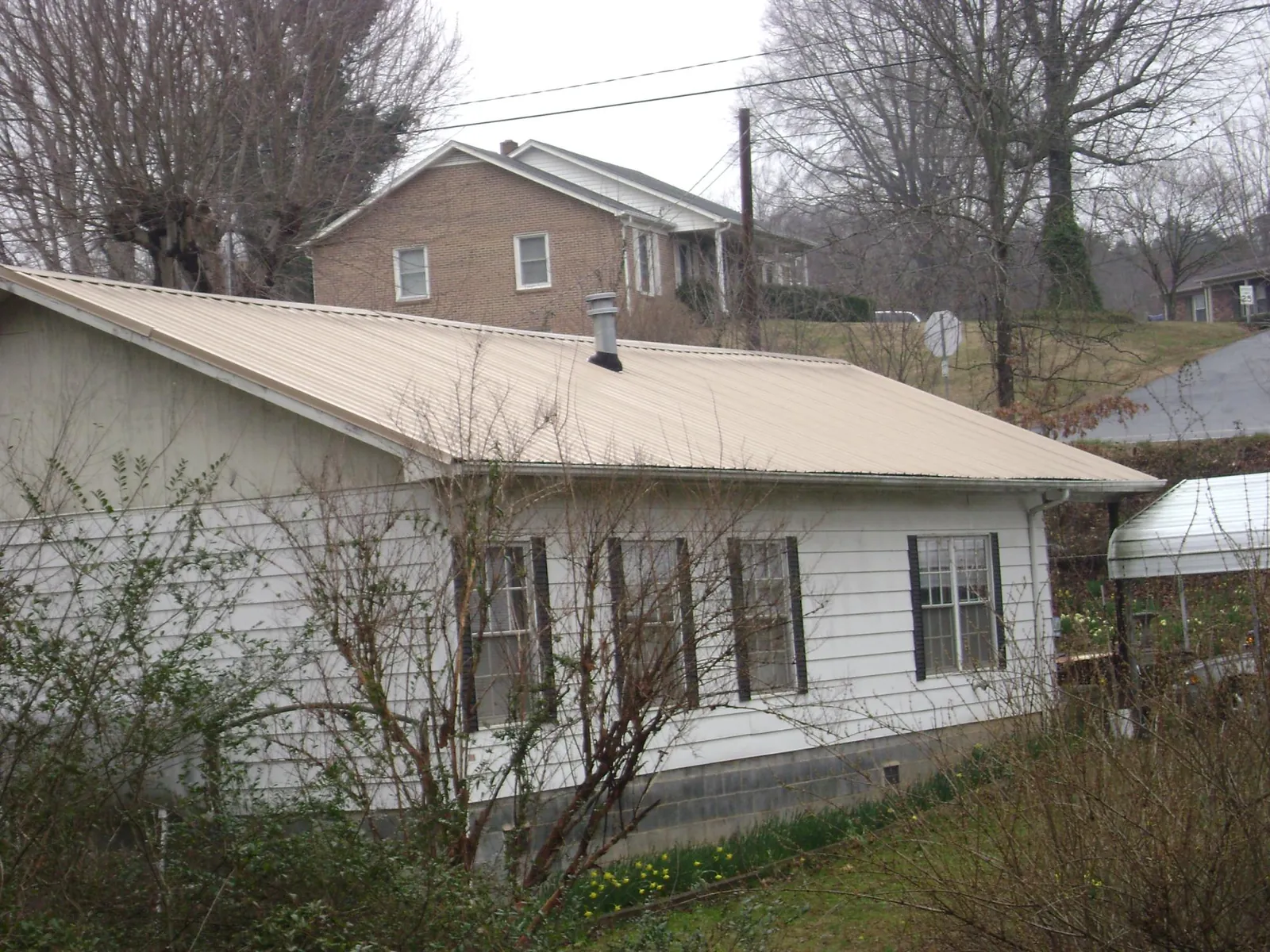 Tan metal roof on a white sided house set into a hillside — Commercial Roofing by Roofing Brothers in Van Hornesville