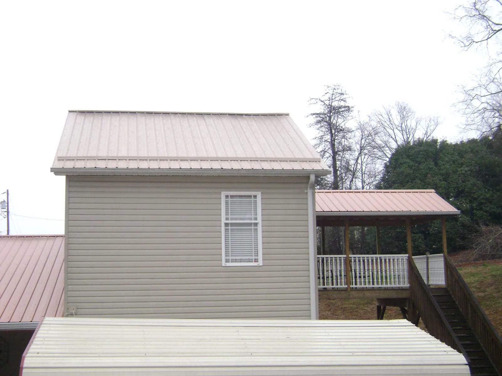 Tan metal roofs on a two story addition and attached porch, from a Roof Replacement job in Van Hornesville